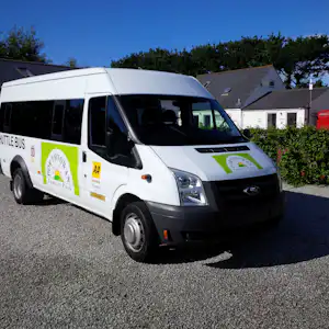 Weißer Campingbus mit grünen Aufklebern steht auf dem Kiesplatz vor weißen Gebäuden und Zelten.