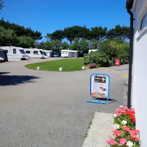 Wohnwagen-Stellplätze auf einem Campingplatz, mit Rasenfläche, Hecken und Blumen vor einem Gebäude.