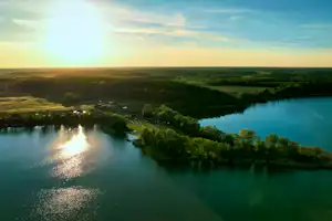 Weitblick auf einen Fluss im Tal mit Uferbäumen und Sonnenlicht am Horizont, aufgenommen aus der Vogelperspektive.