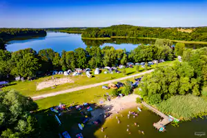 Campingplatz am See mit Zeltplätzen, Rasenflächen und Stegen, umgeben von Bäumen und einem ruhigen Ufer.