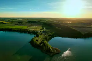 Fluss mit geschwungener Uferlinie, Blick aus der Luft über Felder und Landschaft bei Sonnenuntergang.