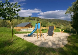 Spielplatz mit Rutsche und Kletterwand auf dem Campingplatz, daneben ein Sandbereich und Wiese mit Bäumen im Hintergrund.