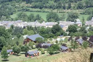Campingdorf mit mehreren Häusern und Zelthütten im Grünen, umgeben von Bäumen und einem grünen Tal im Hintergrund.