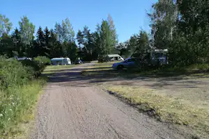 Schotterweg auf einem Campingplatz, umgeben von Bäumen, mit Wohnmobilen und Autos am Rand.