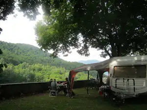Wohnmobil am Campingplatz mit Vorzelt, Campingstühlen und Tisch im Grünen, im Hintergrund Hügel und Bäume.