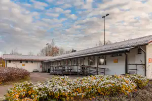 Reihe von Camping-Gebäuden mit überdachter Terrasse, Holzgeländer und Blumenbeeten vor dem Eingang.