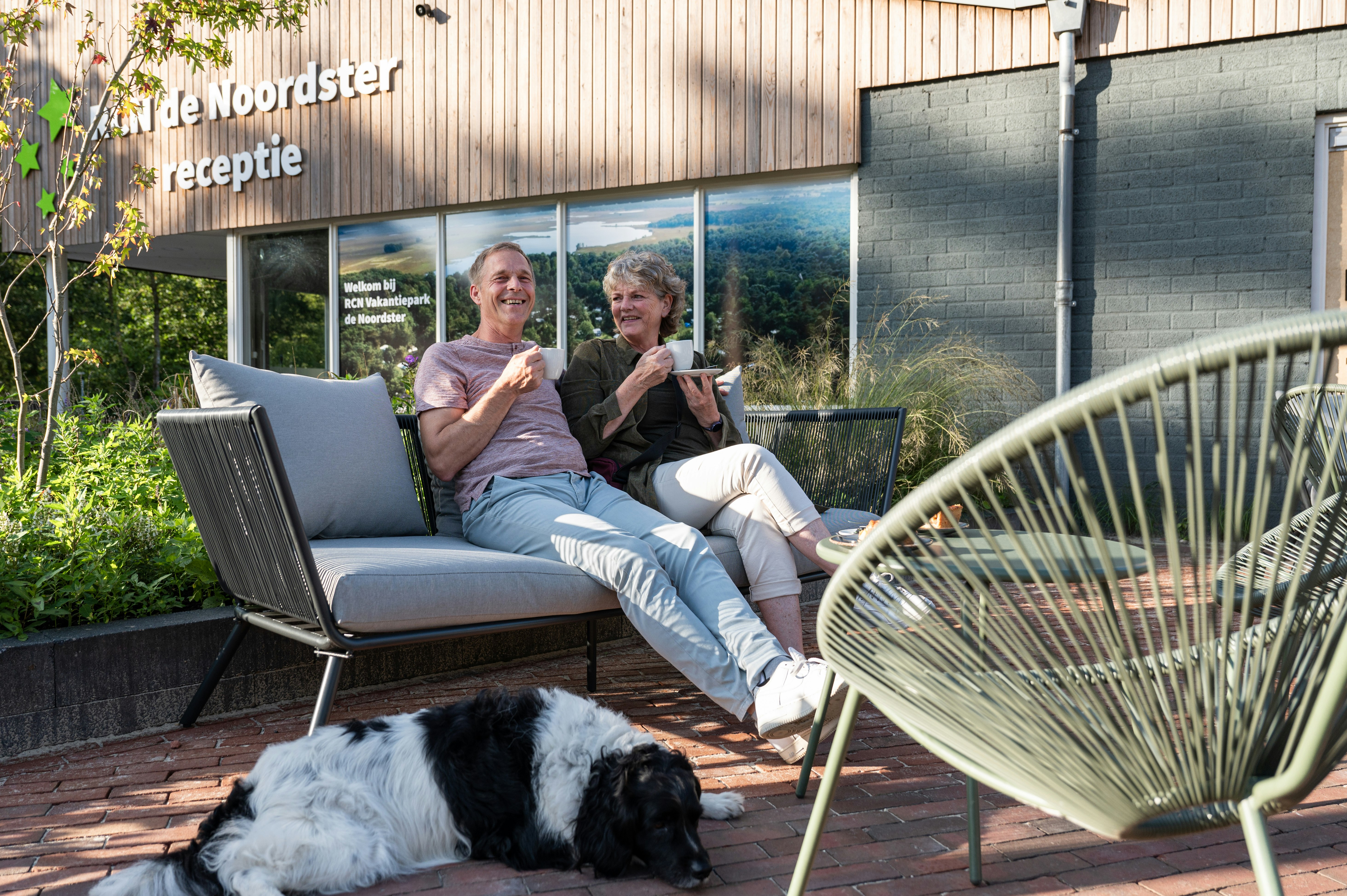 RCN Camping De Noordster - Camper mit Hund genießen einen Kaffee auf der Terrasse des Campingplatzes