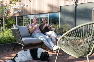 RCN Camping De Noordster - Camper mit Hund genießen einen Kaffee auf der Terrasse des Campingplatzes