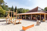 RCN Camping Het Grote Bos - Spielplatz im Sand im Hintergrund Restaurant mit überdachten Sitzmöglichkeiten im Freien