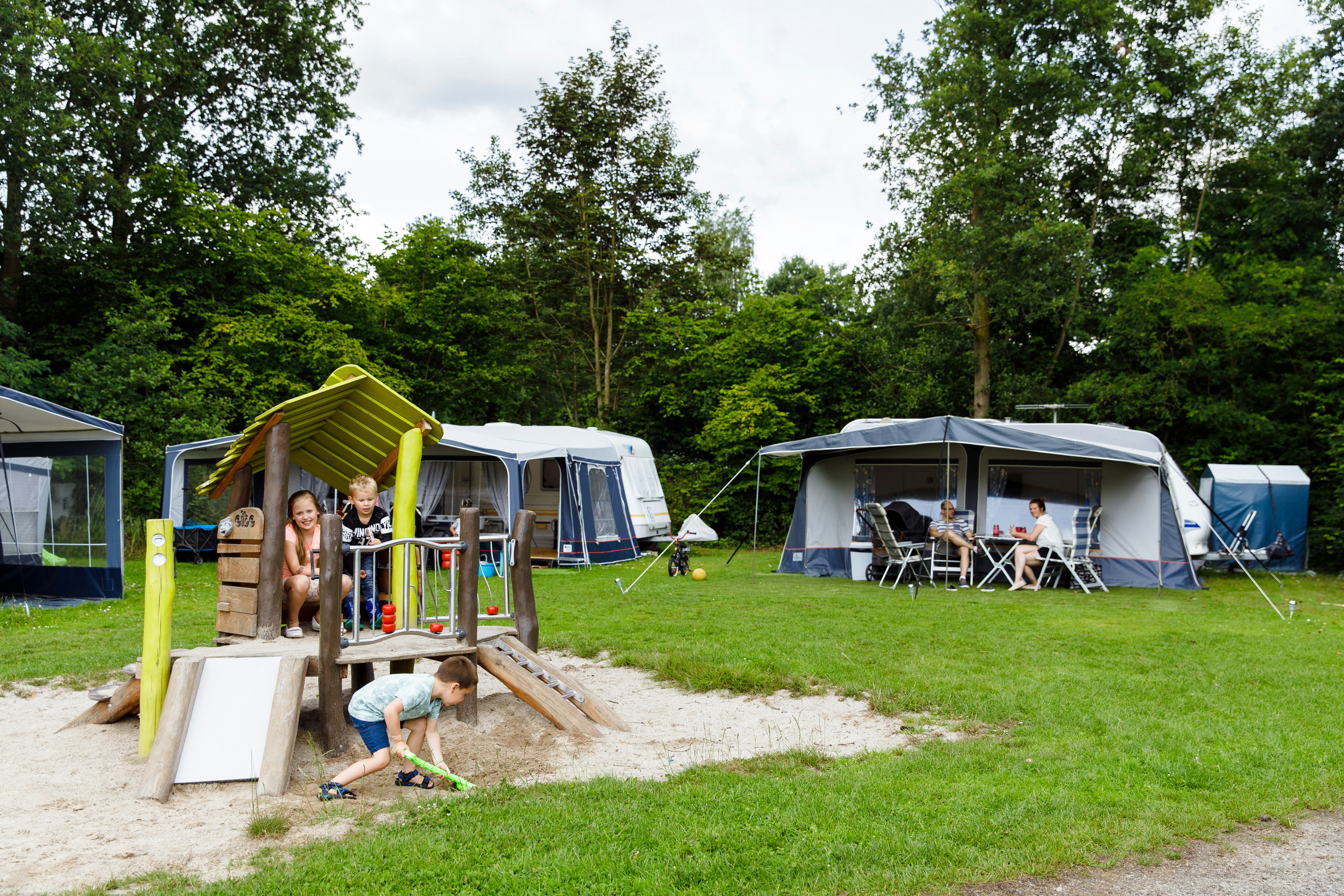 RCN Camping Zeewolde - Stellplatz mit Wohnwagen und einem kleinen Spielplatz davor, auf dem Kinder spielen