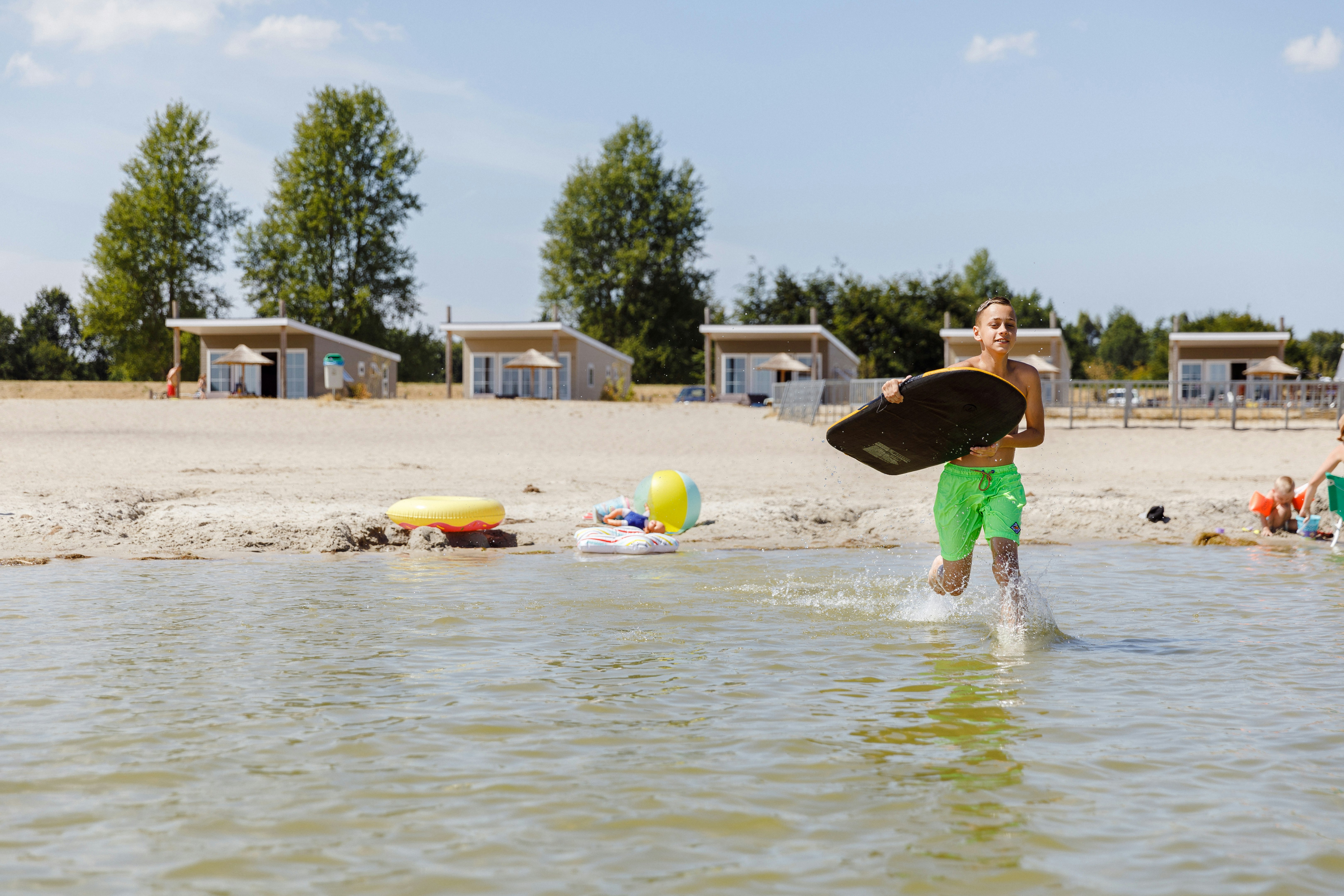 RCN Camping Zeewolde - Strand mit Strandlodges im Hintergrund, im Vordergrund ein surfendes Kind
