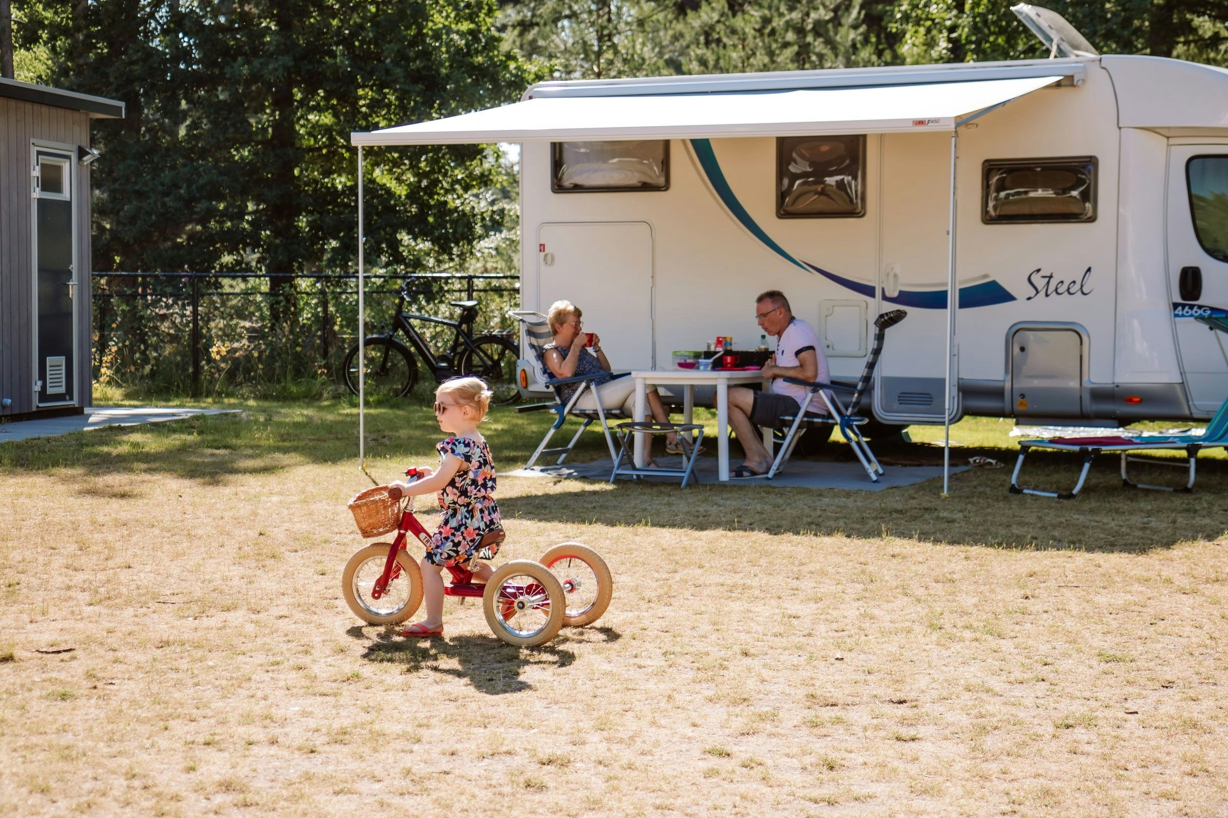 Camping Samoza - Kind fährt Dreirad vor den Standplätzen