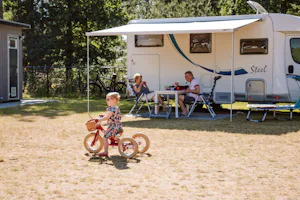 Camping Samoza - Kind fährt Dreirad vor den Standplätzen