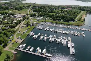 Luftaufnahme eines Campingplatzes am Fluss mit Stegen voller Boote, Parkplätzen, Wegen und grünen Uferbereichen.