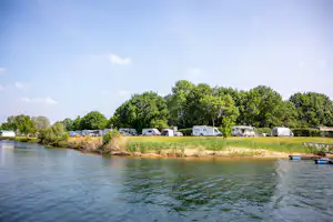 Wohnmobile und Caravans auf dem Campingplatz am See, mit Rasen, Bäumen und Uferpromenade im Hintergrund.