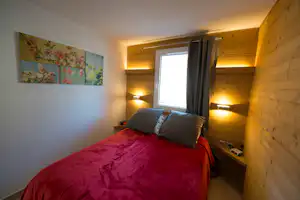 Gemütliches Schlafzimmer im Camping-Bungalow mit Doppelbett, Nachttischen, Lampen und Fenster mit Vorhang.