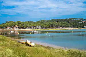 Ufer am See mit Gras, einem kleinen Boot am Strand und einer Reihe Bäume entlang des Wassers.