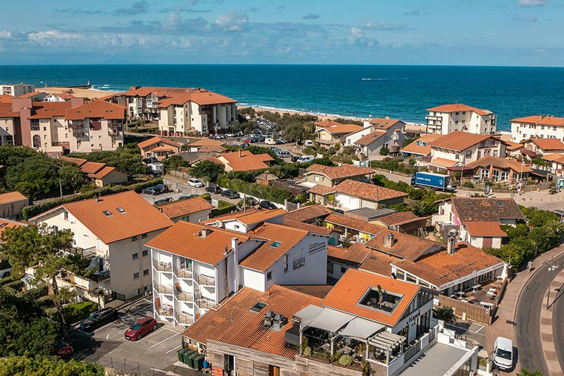 Campinganlage mit Wohngebäuden und roten Ziegeldächern, Straße und geparkten Autos, Blick auf das Meer und die Küste.