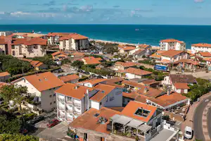 Campinganlage mit Wohngebäuden und roten Ziegeldächern, Straße und geparkten Autos, Blick auf das Meer und die Küste.