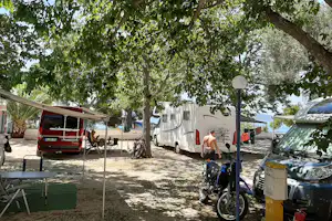 Campingplatz mit Wohnwagen und Wohnmobil, Zelt und Markise unter Bäumen, daneben Fahrrad und Campingausrüstung.