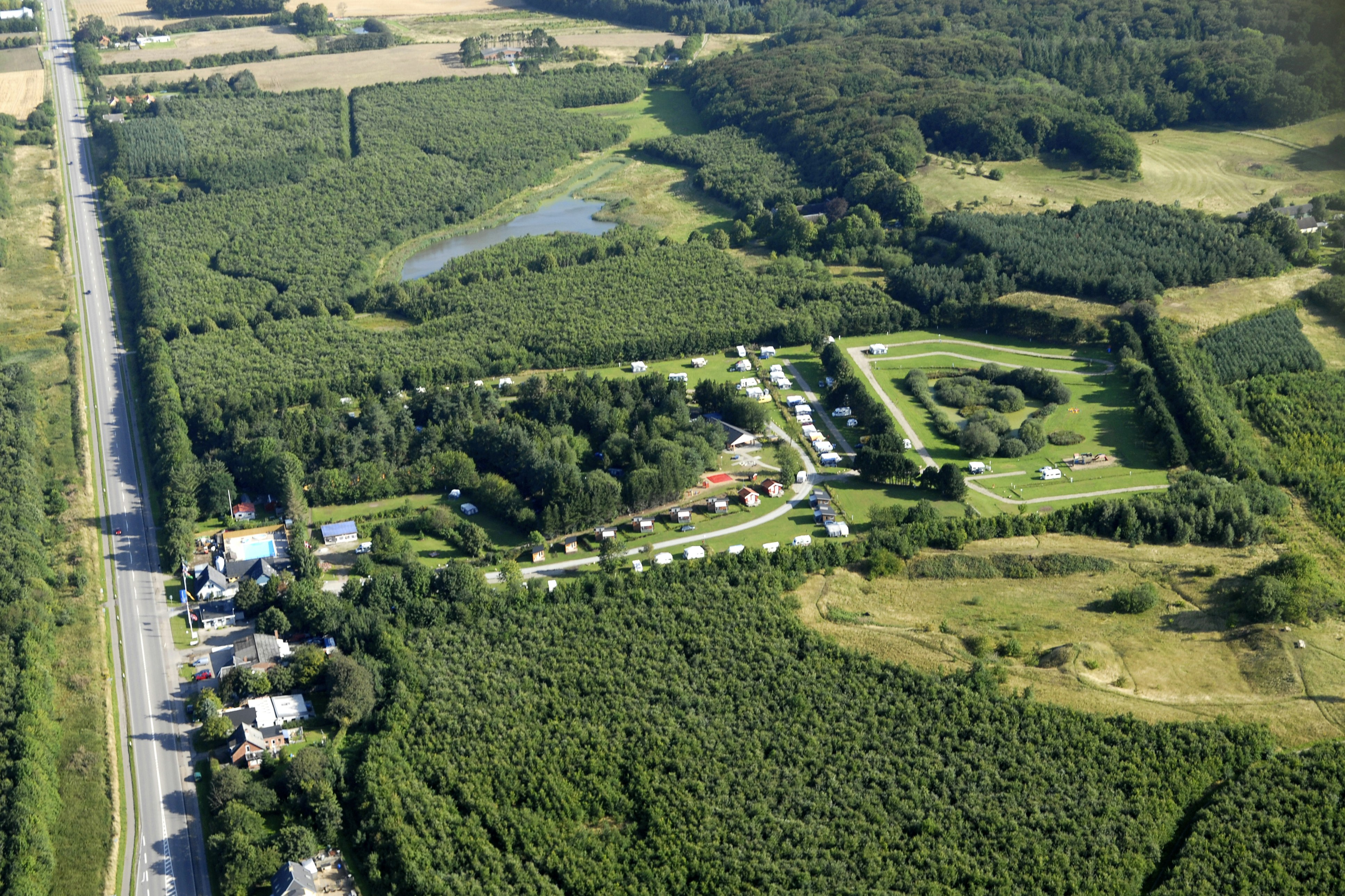 Luftaufnahme einer Campinganlage im Grünen mit Wegen, Stellplätzen und mehreren Gebäuden inmitten von Feldern und Wäldern.
