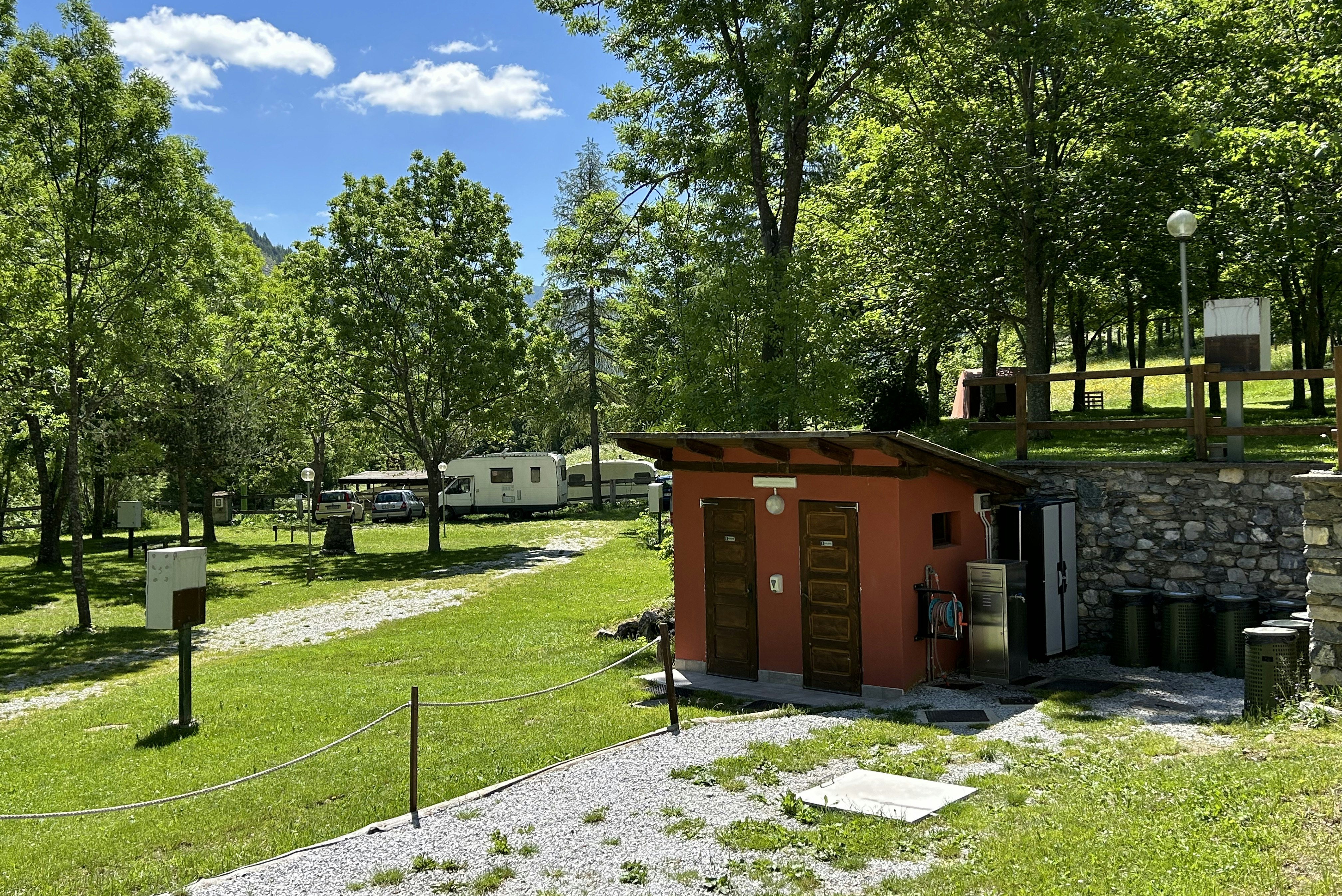 Grüne Campinganlage mit Wohnwagen und Autos auf dem Stellplatz, im Vordergrund ein kleines Gebäude am Steinmauerbereich.