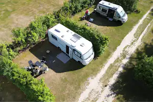 Wohnmobil auf einem Stellplatz mit Vorzelt und Sitzgruppe, daneben ein weiteres Fahrzeug, umgeben von Bäumen und Rasen.