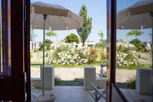 Blick von der Camping-Terrasse mit Markise auf einen gepflegten Garten mit Blumenbeeten und Sitzbank.