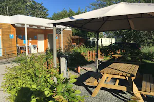 River Camping Prague - Picknicktisch unter Sonnenschirm und Sanitärgebäude vom Campingplatz