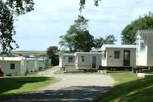 Reihen von Wohnwagen auf einem Campingplatz, mit Rasenflächen, Wegen und Bäumen im Hintergrund.
