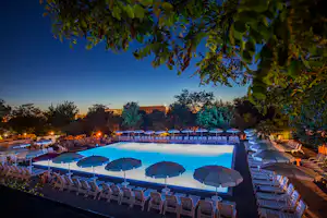 Roma Camping - Poolbereich vom Campingplatz mit Sonnenschirmen und Liegestühlen am Abend