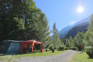 Campingzelt mit rotem Eingang auf dem Stellplatz, umgeben von Bäumen und Blick auf bewaldete Berge im Tal.