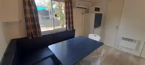 Wohnbereich mit Sofa und Esstisch, daneben Schrank und Tür, große Fensterfront mit Blick auf den Außenbereich.