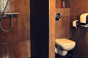 Camping-Badezimmer mit WC, Duschkopf und Vorhang an einer Holzverkleidung, daneben Handbrause und Wandarmatur.