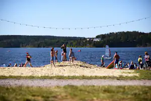 Kinder am Seeufer am Sandstrand, im Hintergrund Boote und eine lange Lichterkette über dem Wasser.