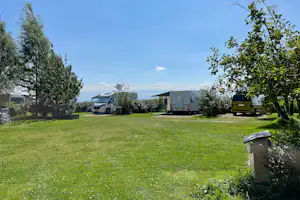 Wohnmobile auf einer grünen Wiese im Campinggarten, mit Bäumen, Markise und mehreren Fahrzeugen nebeneinander.