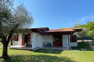 Bungalow mit Terrasse, Sitzgruppe und Markise, umgeben von Rasen und Bäumen im Campingbereich.