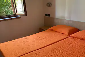 Schlafzimmer in einer Campingunterkunft mit zwei Betten, orangefarbenen Decken und Fensterblick ins Grüne.