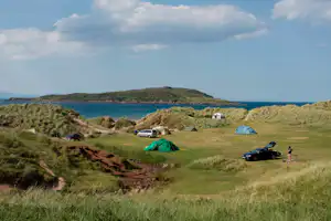 Campingplatz am Meer mit grünen und blauen Zelten, Autos und Wohnmobil nahe Dünen und Küste.