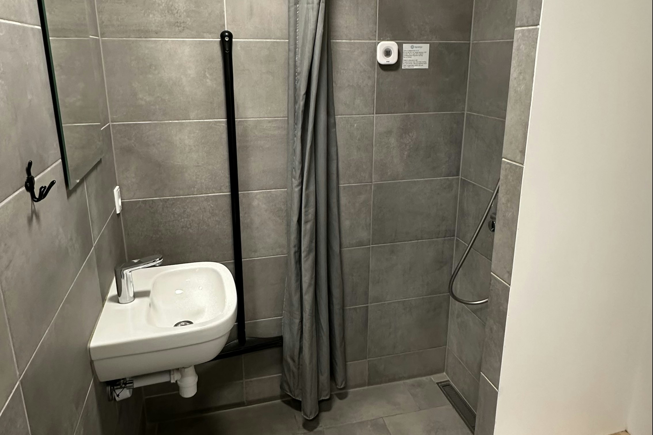 Modernes Badezimmer mit Dusche, Duschvorhang, WC und Waschbecken, grauen Fliesen und Wandhandtuchhalter.