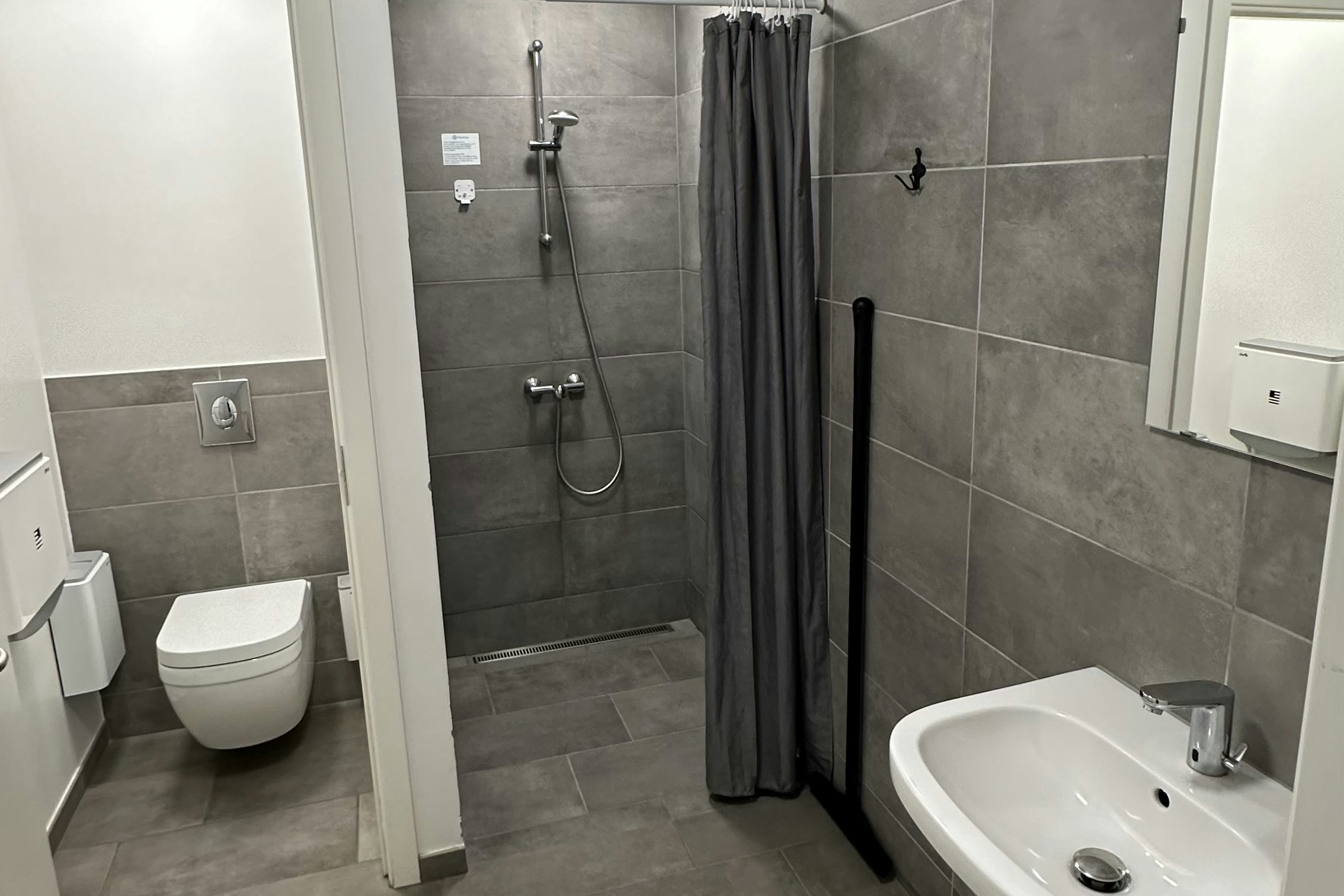Modernes Camping-Badezimmer mit grauen Fliesen, Waschbecken, WC und Dusche mit Vorhang.