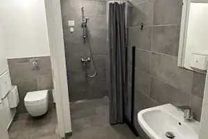 Modernes Camping-Badezimmer mit grauen Fliesen, Waschbecken, WC und Dusche mit Vorhang.