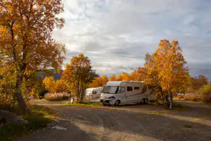 Wohnmobil auf einem Stellplatz am Campingplatz, umgeben von bunten Herbstbäumen und einem breiten Weg.