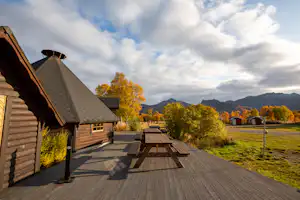 Holzhütten und eine große Holzterrasse am Campingplatz, Blick auf Berge und gelbe Bäume im Herbst.
