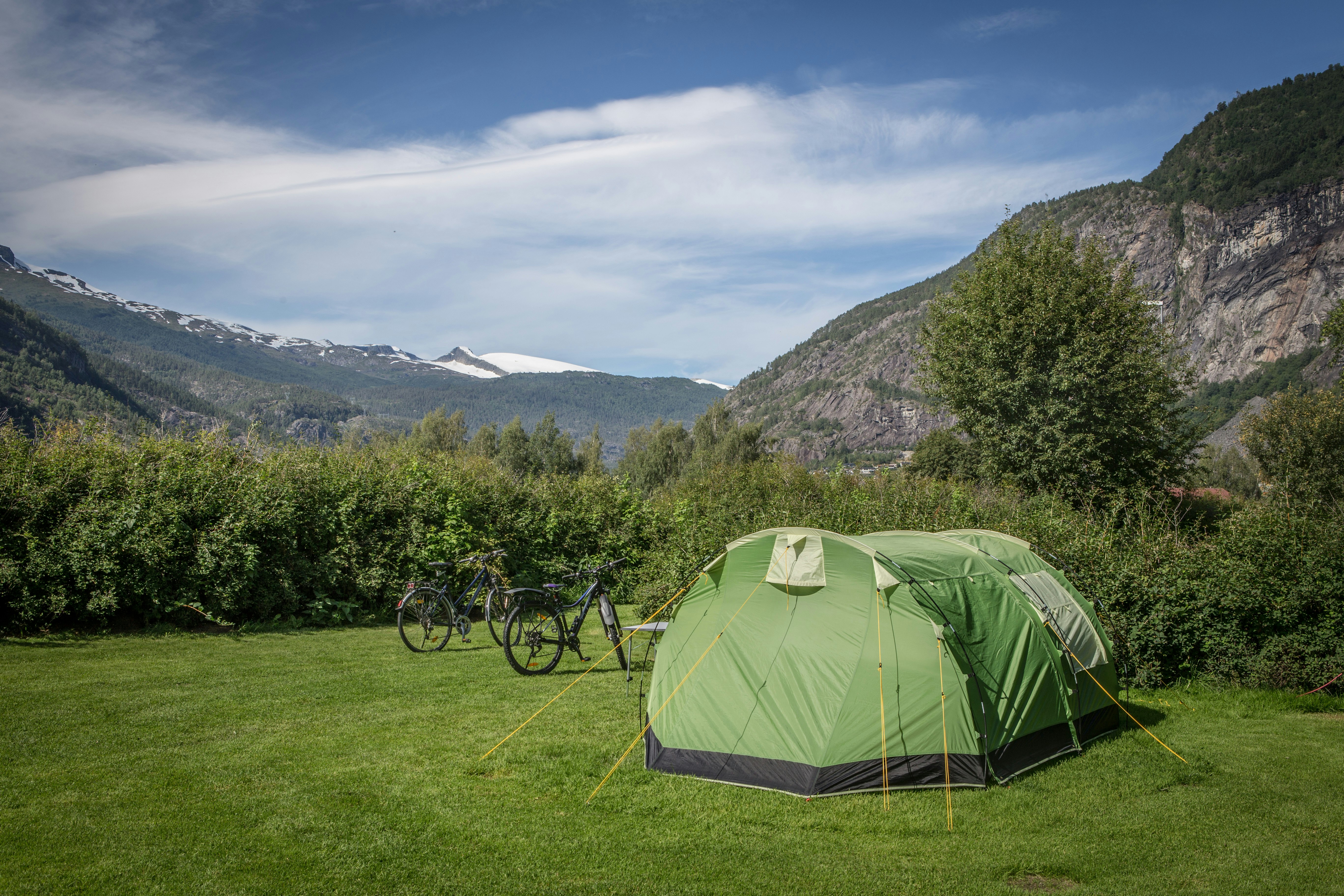 Grünes Zelt auf einer Wiese im Campingplatz, Fahrräder daneben, umgeben von Bergen und Bäumen im Tal.