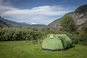 Grünes Zelt auf einer Wiese im Campingplatz, Fahrräder daneben, umgeben von Bergen und Bäumen im Tal.