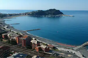Blick auf eine Küstenbucht mit Hafen, Booten und Wohnhäusern am Meer.