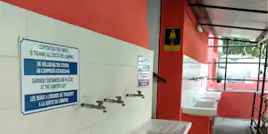 Hinweisschild an der Wand im Sanitärbereich, daneben Waschbecken und Wasserhähne in einem roten Gebäude.