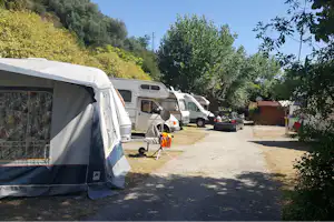 Wohnwagen und Campingbusse auf dem Stellplatz, Zeltvorderseite im Vordergrund, Autos und Bäume am Rand.