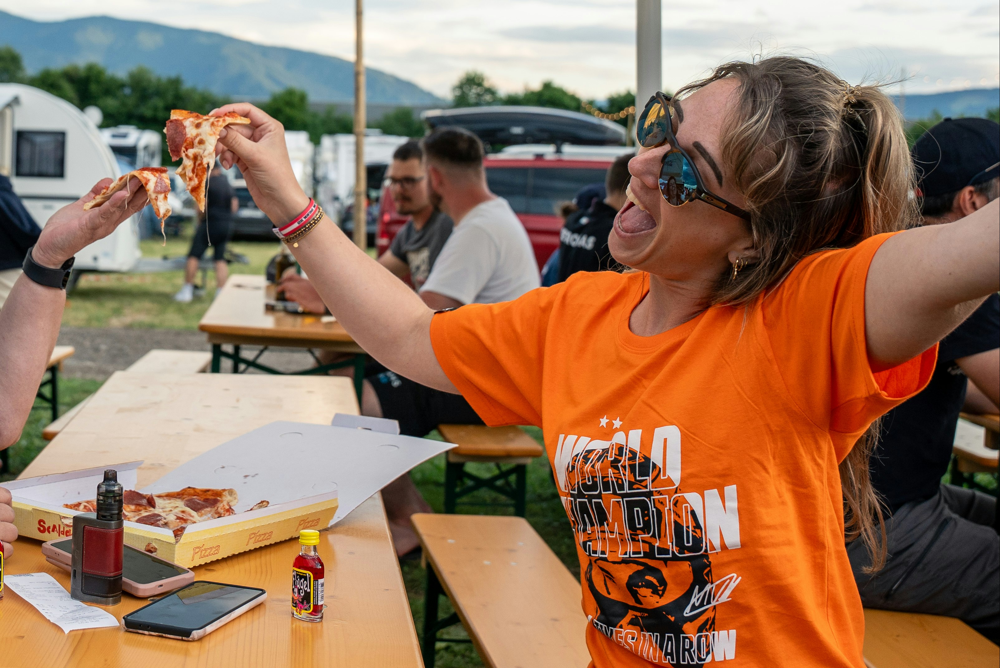 Schitterhof Camping - Camper essen gemeinsam Pizza auf Bierbänken auf dem Campingplatz